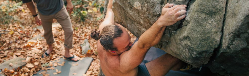 person climbing a large boulder outdoors.