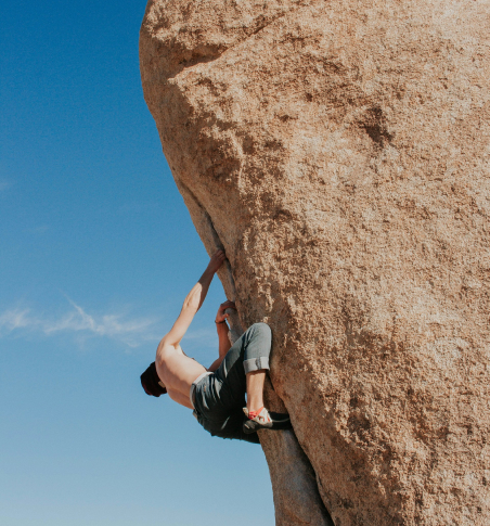 a person climbing a large boulder outdoors with a blue sky in the background
